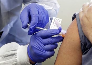 Neal Browning receives a shot in the first-stage safety study clinical trial of a potential vaccine for COVID-19, the disease caused by the new coronavirus, Monday, March 16, 2020, at the Kaiser Permanente Washington Health Research Institute in Seattle. Browning is the second patient to receive the shot in the study. (AP Photo/Ted S. Warren)